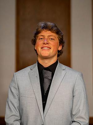 White man with light brown hair wearing a black dress shirt and grey suit jacket